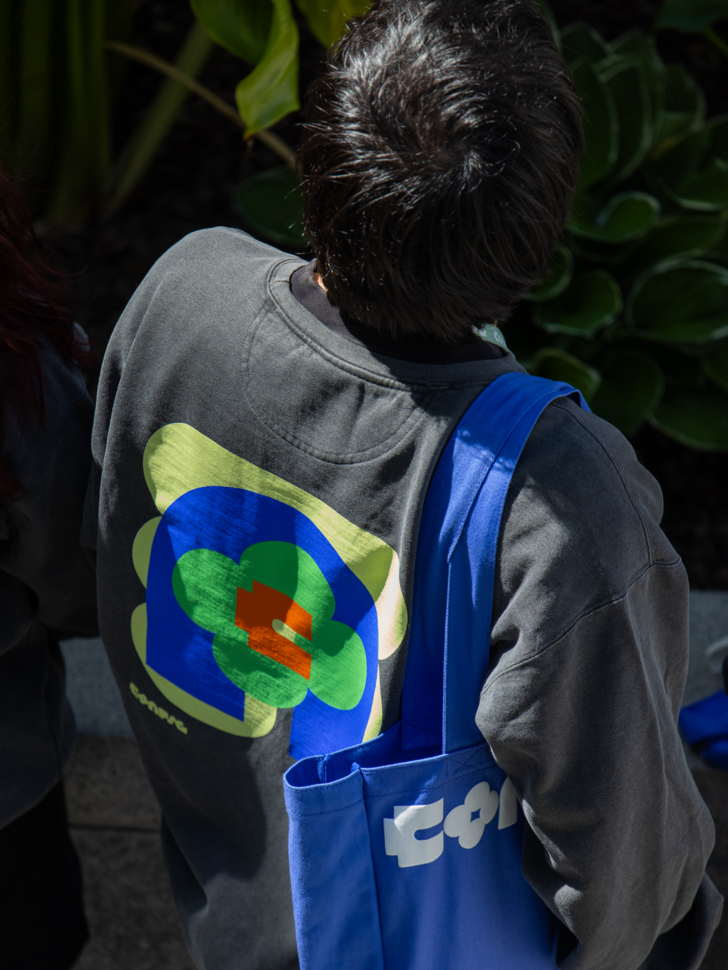 Person with back turned wears sweatshirt and Figma Config tote featuring colorful abstract conference design.