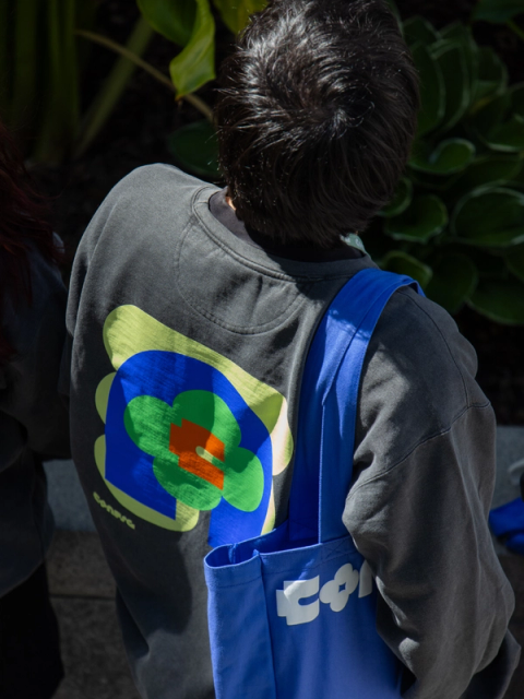 Person with back turned wears sweatshirt and Figma Config tote featuring colorful abstract conference design.