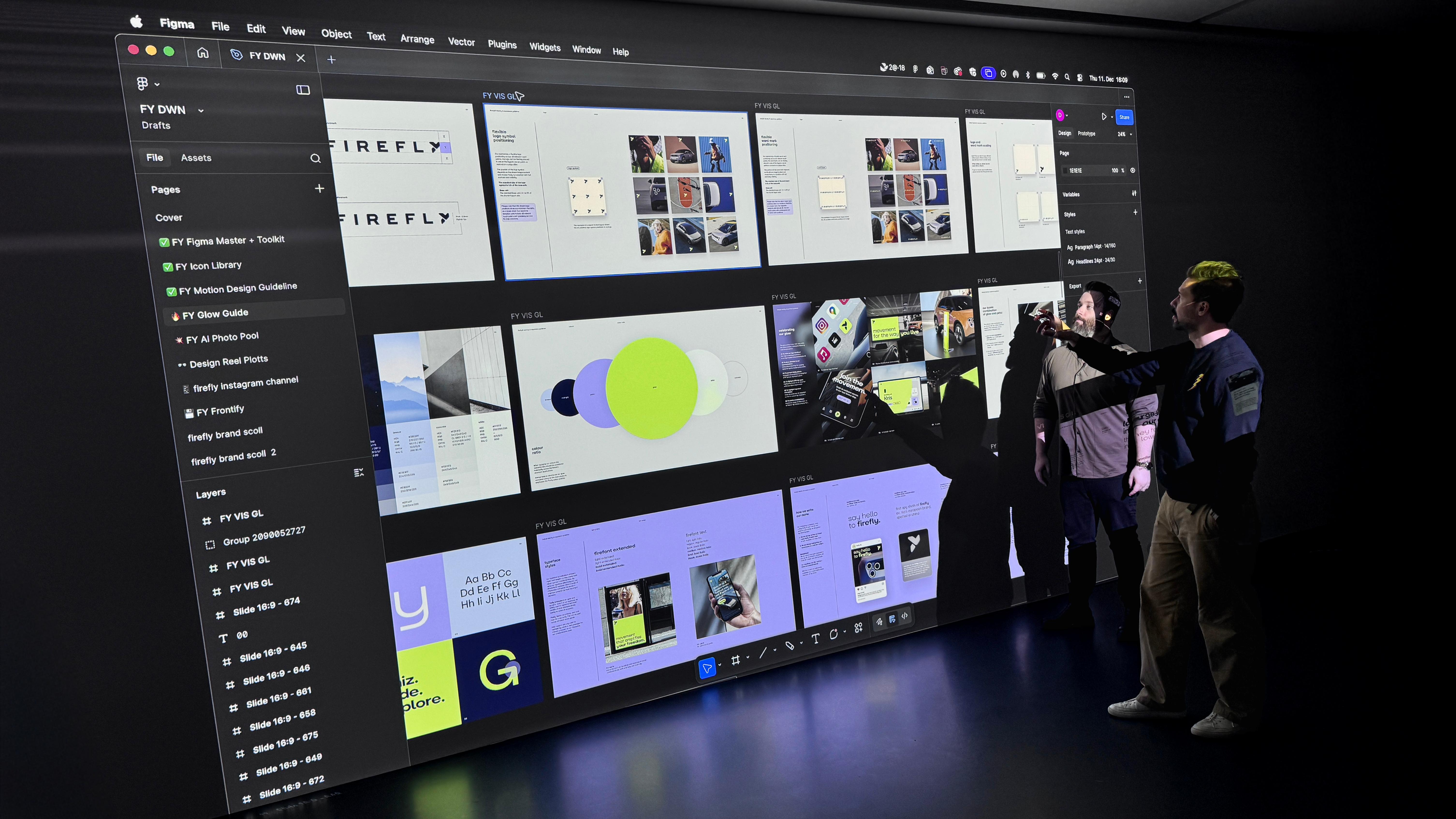 two people looking at a large screen with figma file and screens of interface displayed