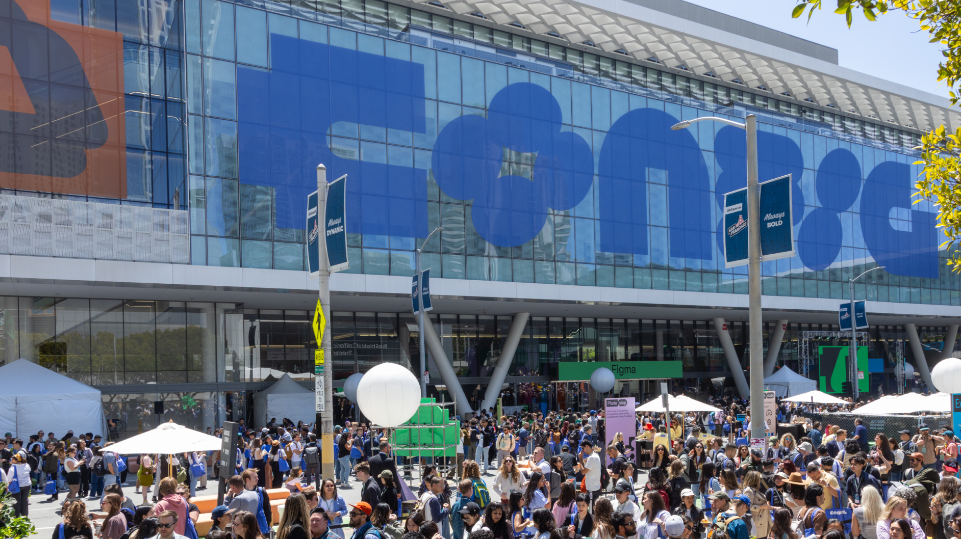 Large crowd gathers outside a convention center with massive blue “Config” banner on glass facade.