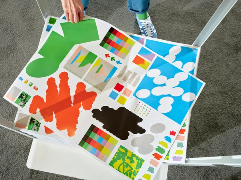 A hand picks up a printed reference poster showing color palettes and organic shapes