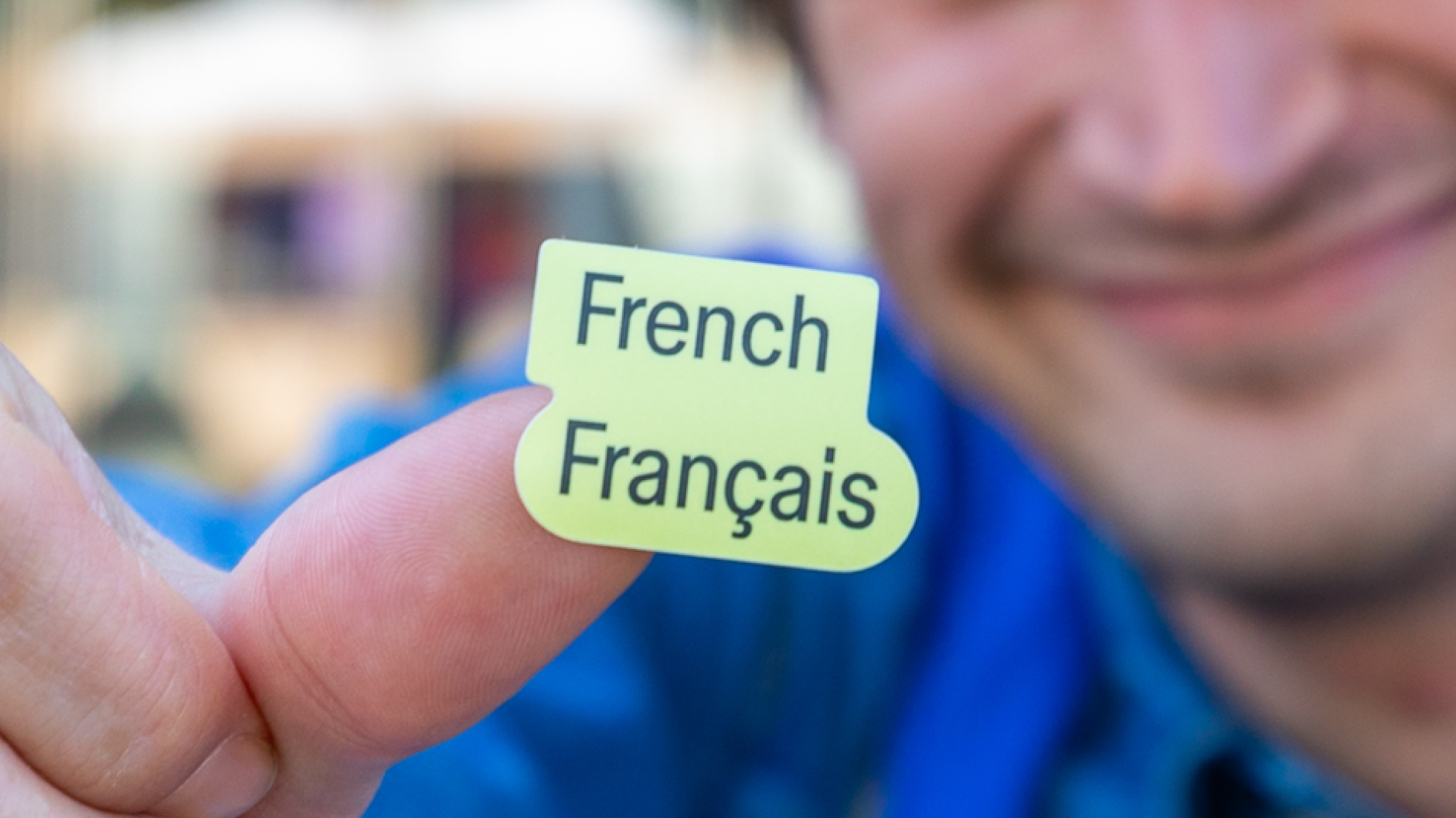 Smiling person holds a bright green “French / Français” sticker