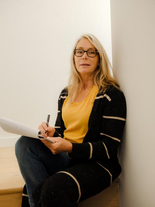 A portrait of Michele Scott, a white blonde woman, sitting at the top of the stairs