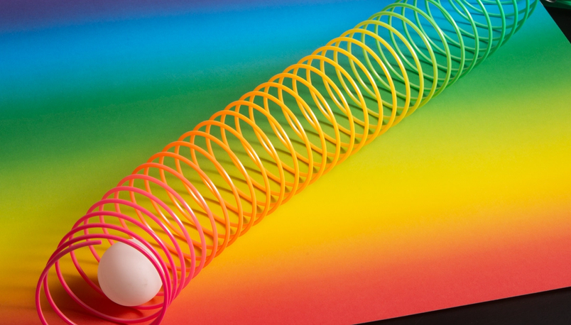 Slinky en plastique aux couleurs de l'arc-en-ciel étiré sur une feuille à dégradé vibrant avec un œuf à l'une des extrémités.