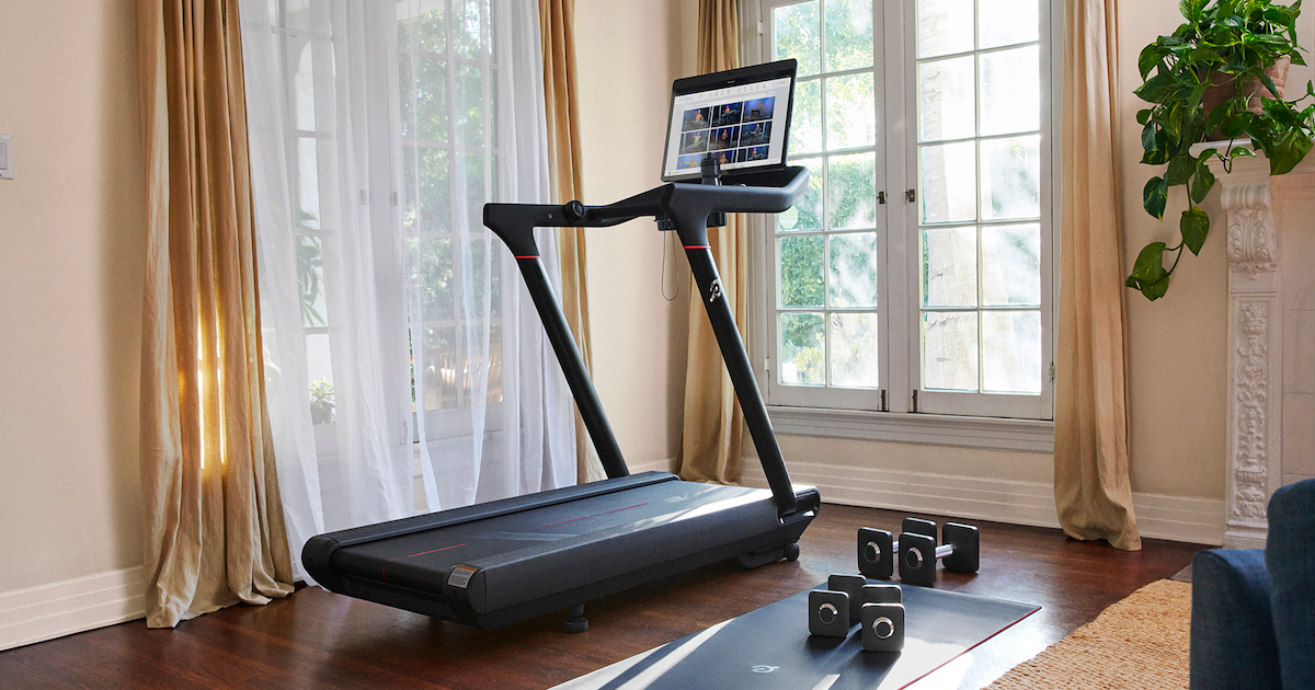 Peloton treadmill in living area with mat and weights on the ground next to it