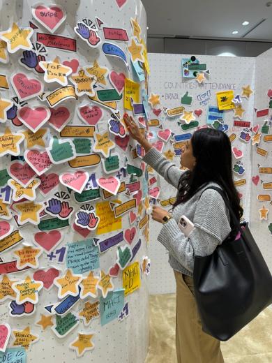 A woman places a star-shaped sticky note on a white wall covered with other notes.