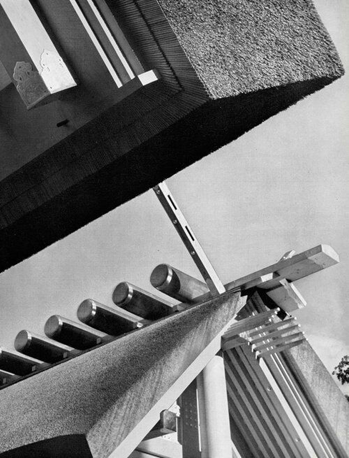 Black and white architectural photograph showing dramatic angles of a modernist building with exposed beams, concrete surfaces, and strong shadow contrasts.