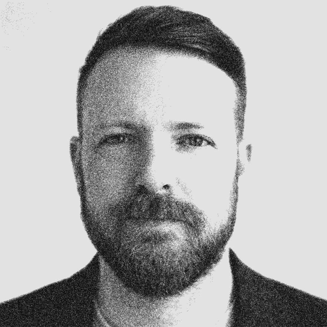Bearded man with short hair, wearing jacket, black and white closeup portrait against plain background
