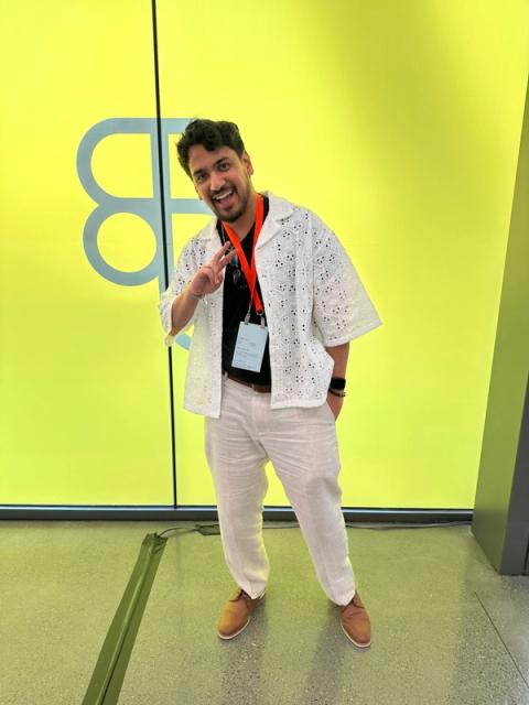 A man wears an open white lace shirt over a black tee and white pants