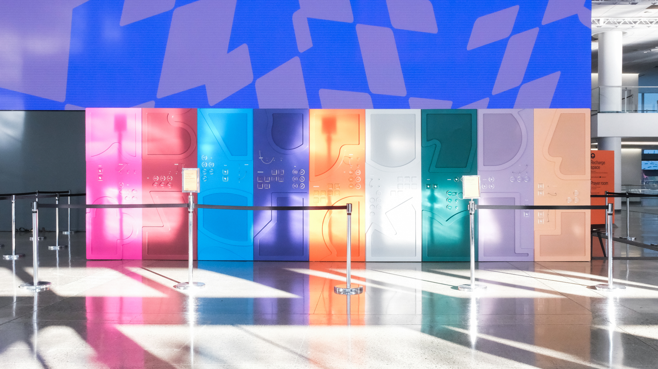 Colorful interactive wall with abstract shapes and buttons lit by sunlight in a Config convention hallway.