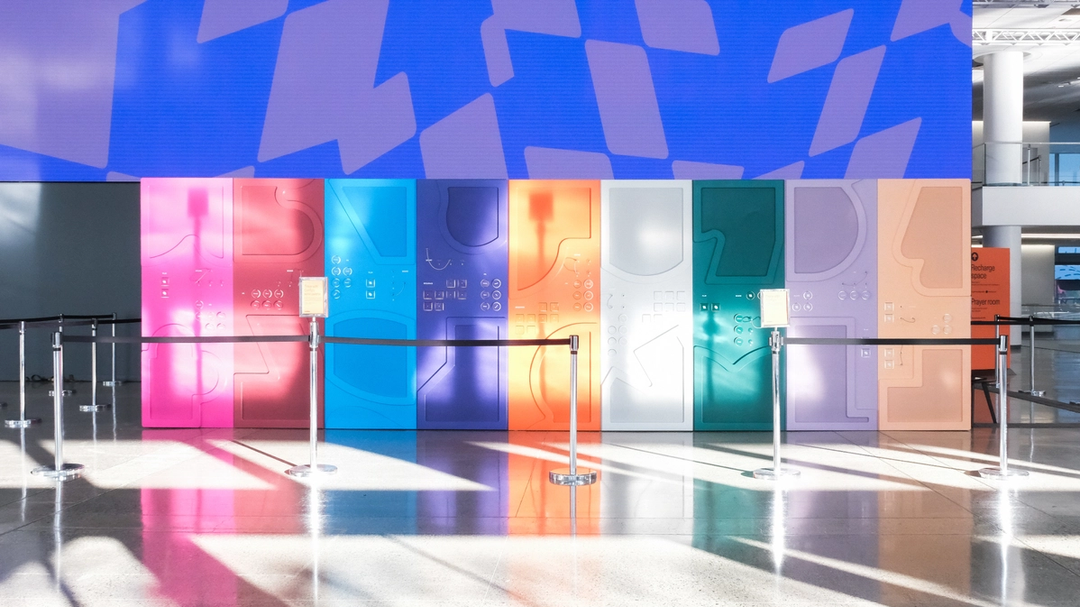 Colorful interactive wall with abstract shapes and buttons lit by sunlight in a Config convention hallway.