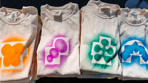Four folded white t-shirts display spray-painted Config icon designs in orange, purple, green, and blue.