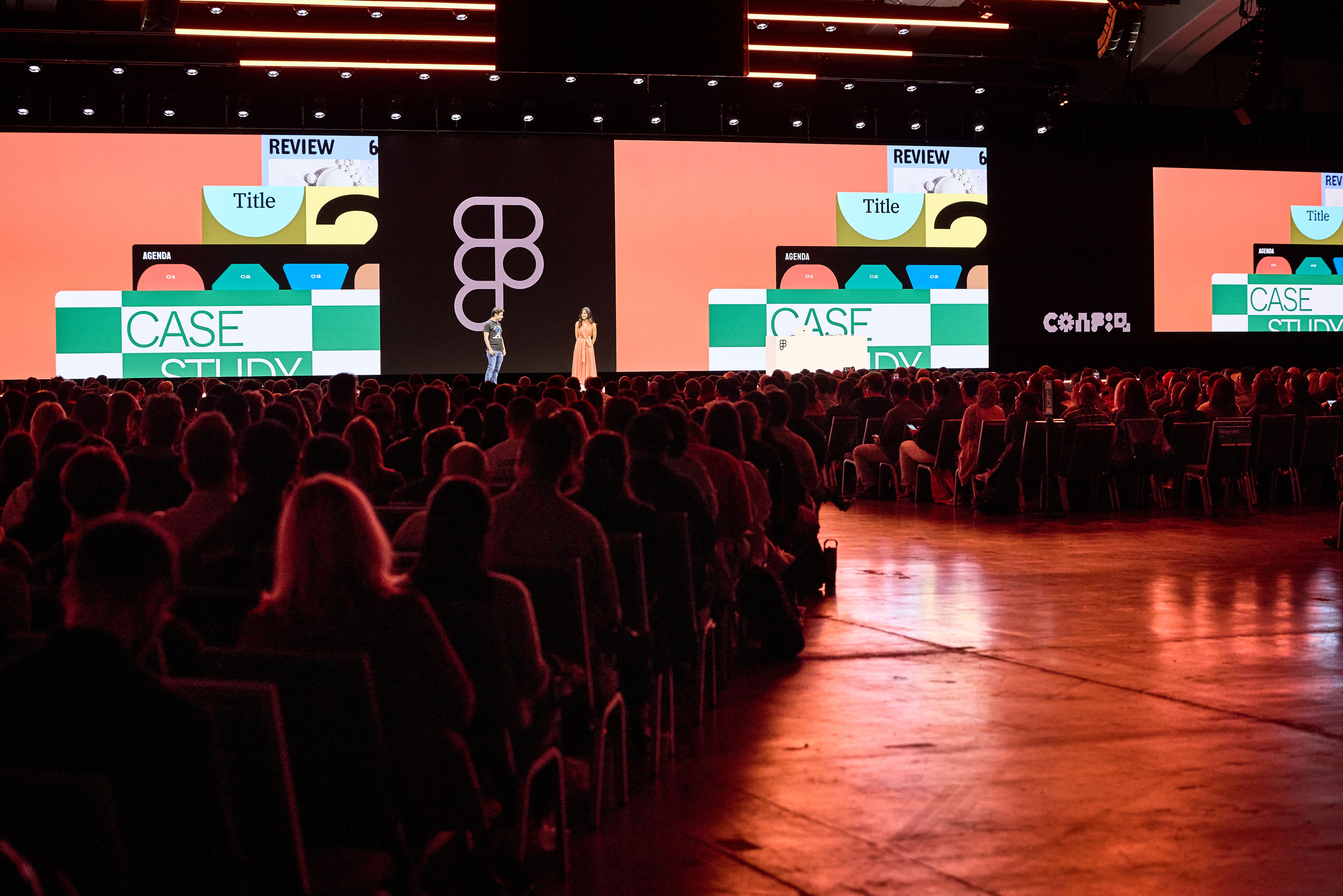 A wide view of a crowded auditorium with a presenter on stage. Large screens behind the presenter show a colorful slide with the title "Case Study" and Figma branding.