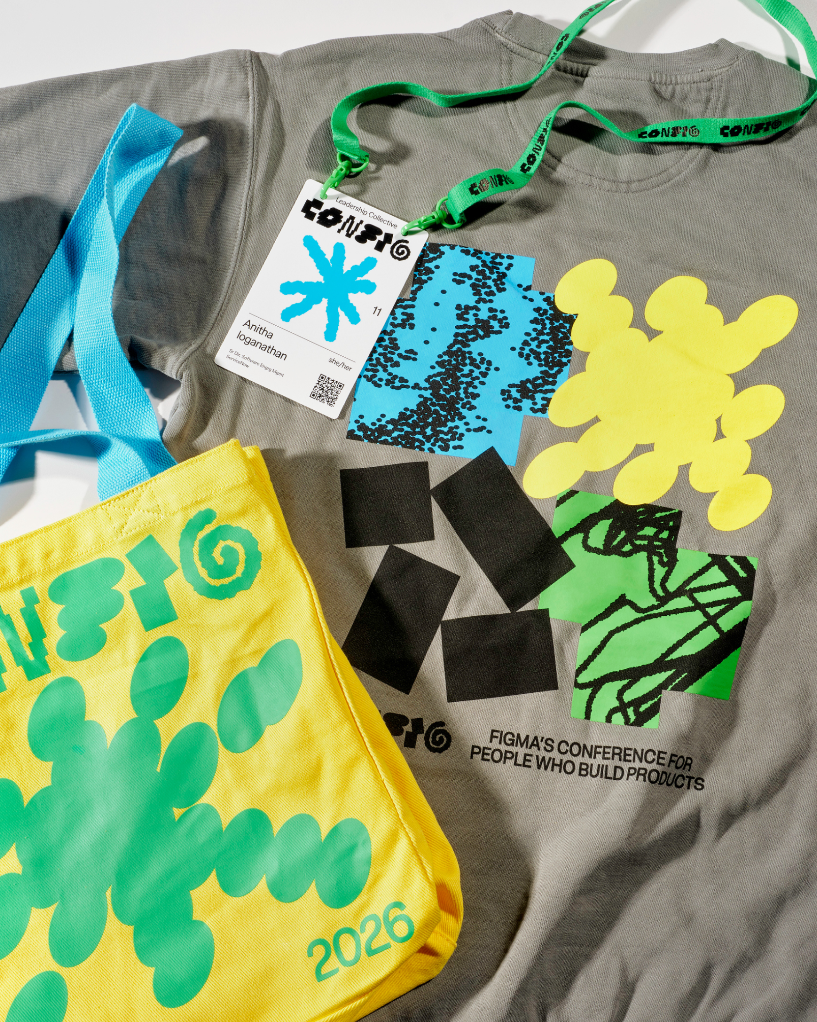An arrangement of a yellow Config tote bag, gray sweater, and conference badge.