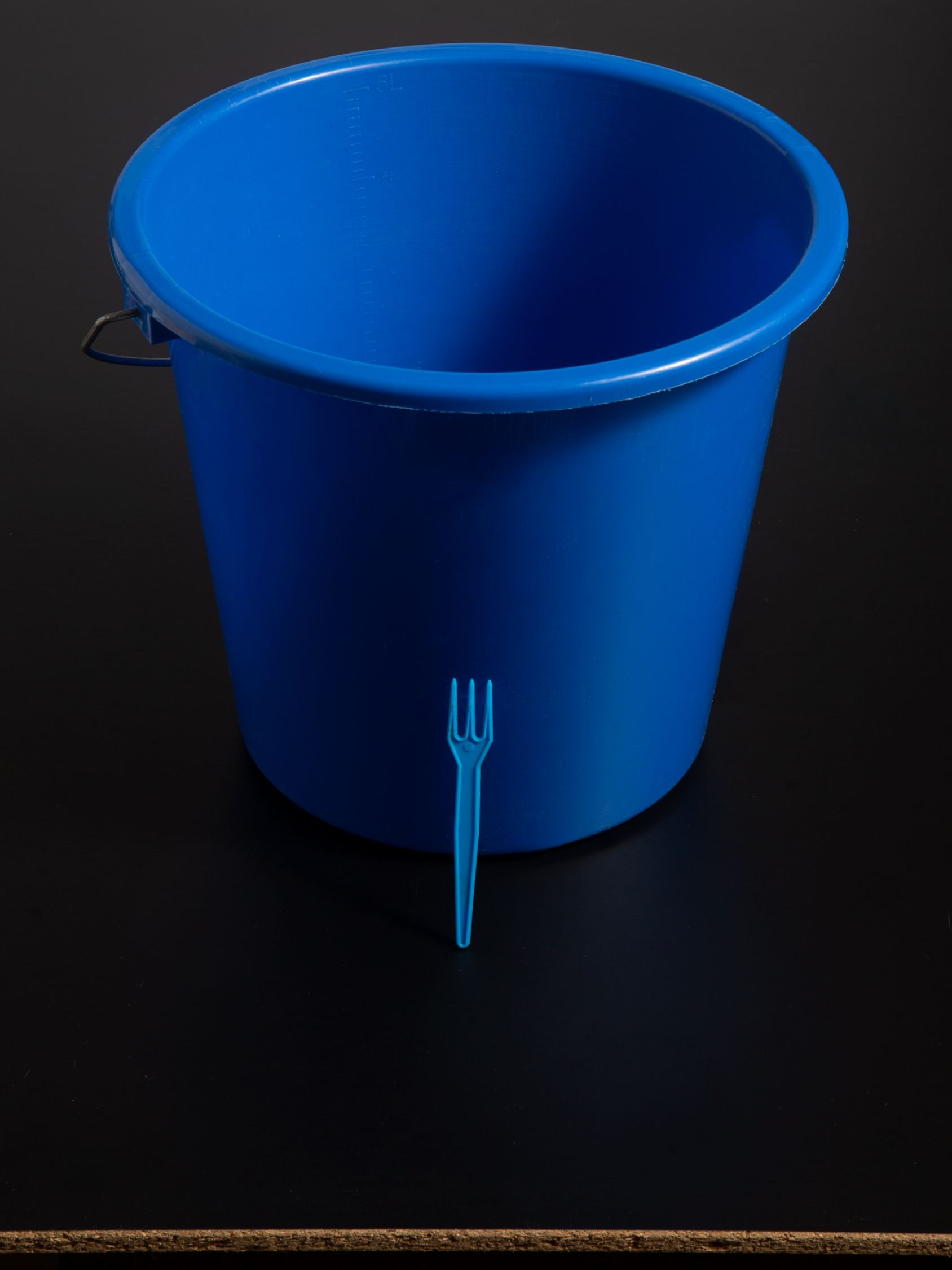 Large blue plastic bucket with a small blue fork leaning against it.