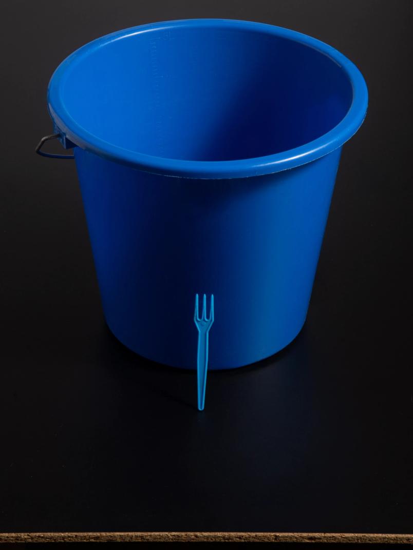 Large blue plastic bucket with a small blue fork leaning against it.