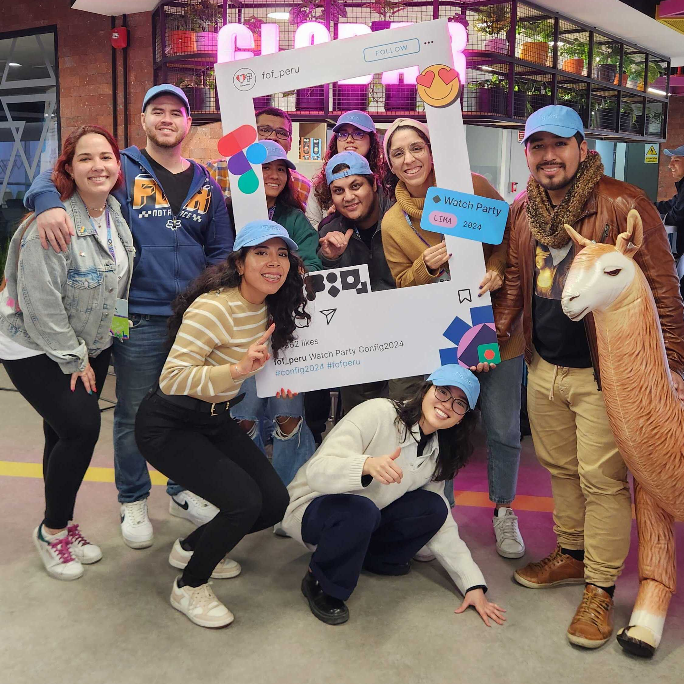 A group of people posing together at an event, wearing blue caps and holding a large Instagram-style frame prop. The frame displays text referencing "fof_peru," "Watch Party," "Lima 2024," and hashtags like "#config2024" and "#fofperu." One person is holding a llama figure. The setting appears to be an indoor venue with colorful decor.