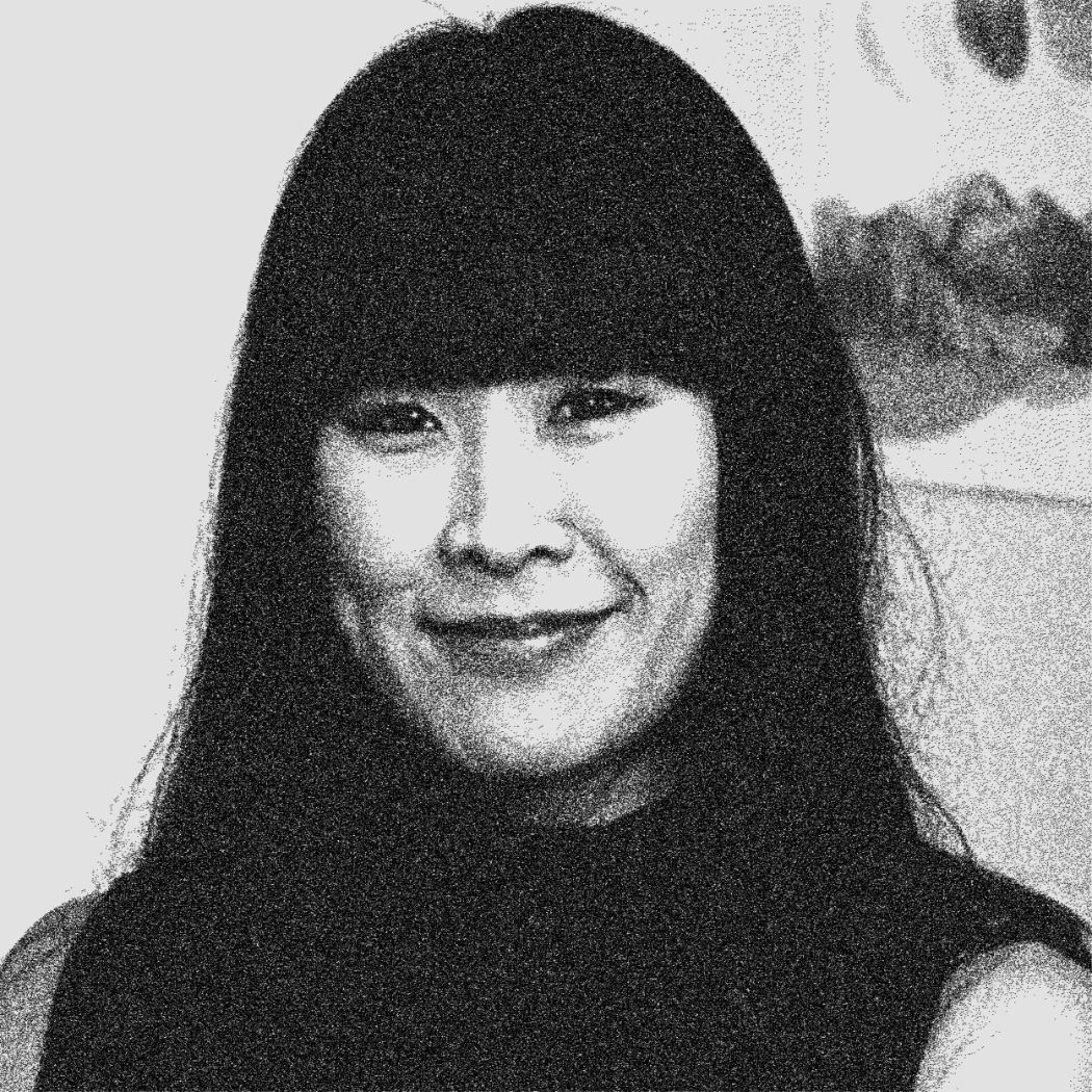 Woman with long dark hair and bangs, smiling slightly, black and white portrait indoor background.