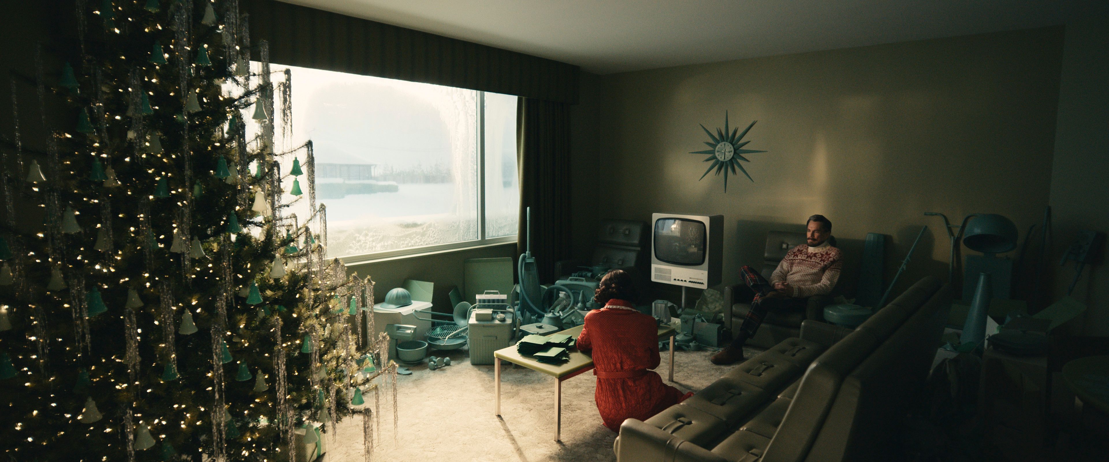 A vintage-style living room with a Christmas tree is filled with teal household items as a man and woman sit in quiet contemplation.