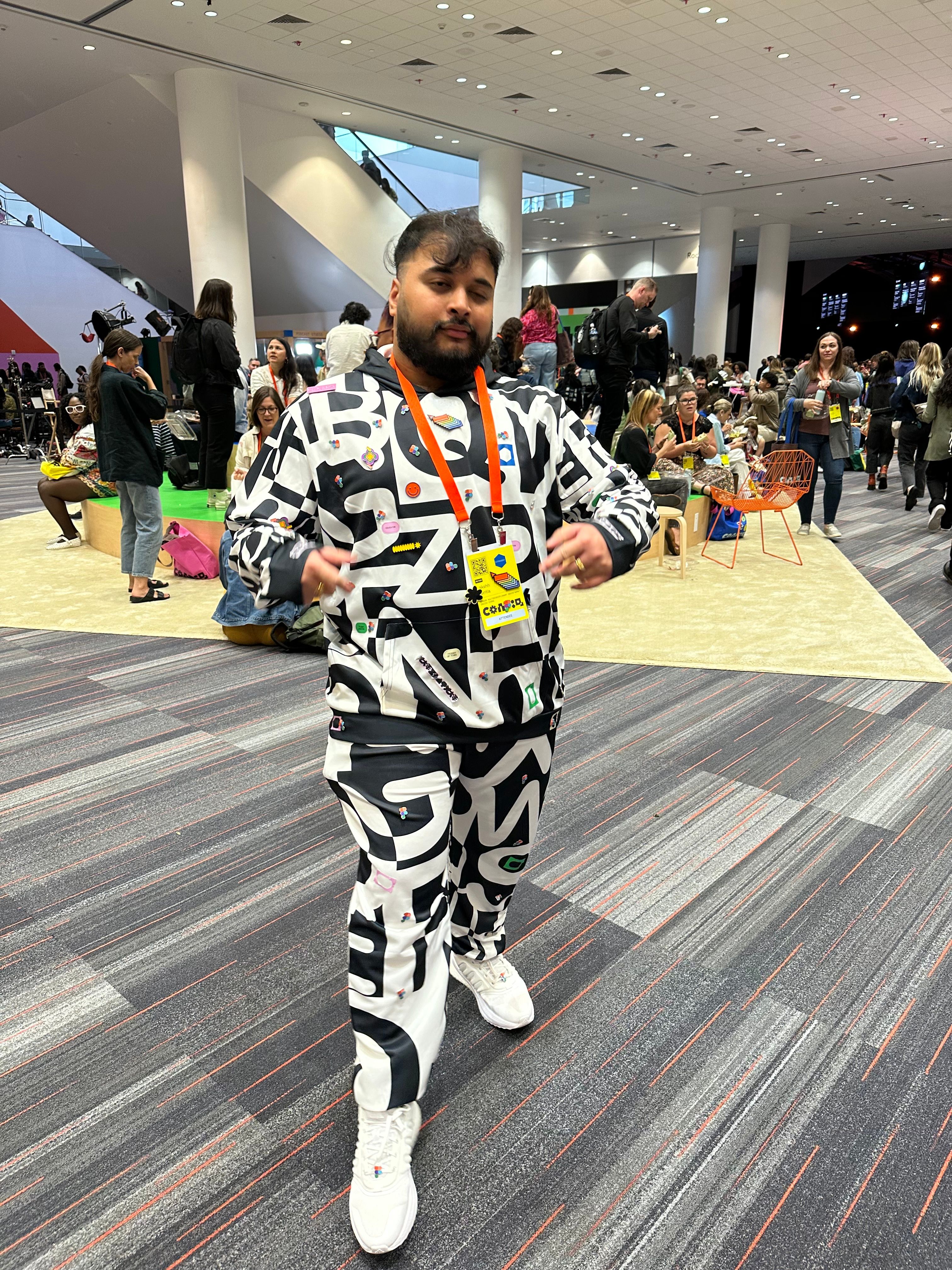 A man wears a tracksuit set on bold typographic print textile. There are pins fastened all over the top and botoms.