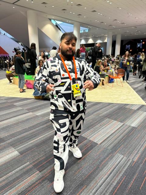 A man wears a tracksuit set on bold typographic print textile. There are pins fastened all over the top and botoms.