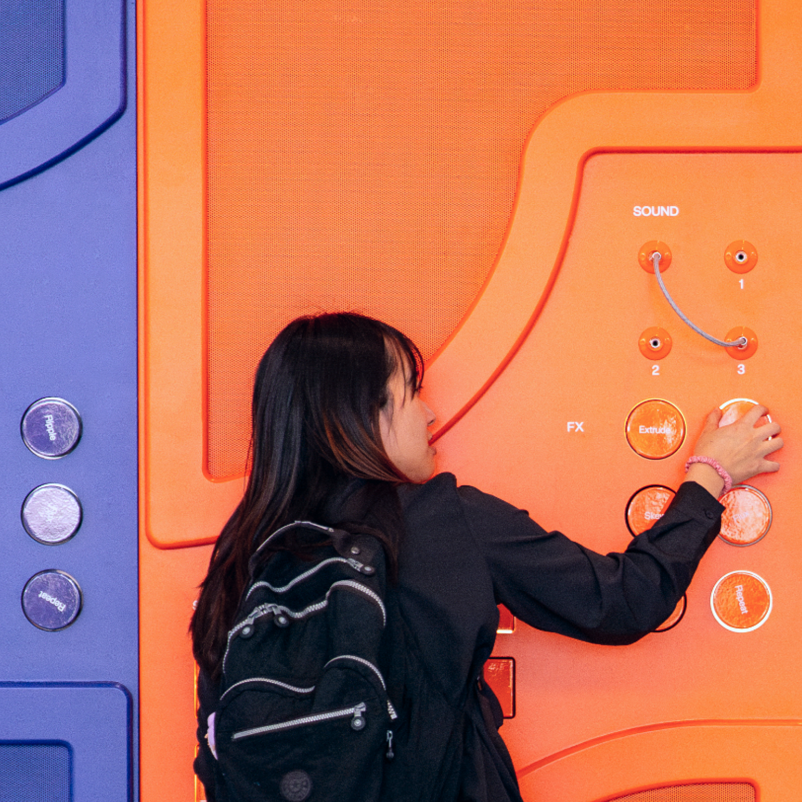 Attendee with backpack interacts with bright orange FX panel labeled “Sound” on Config event wall.