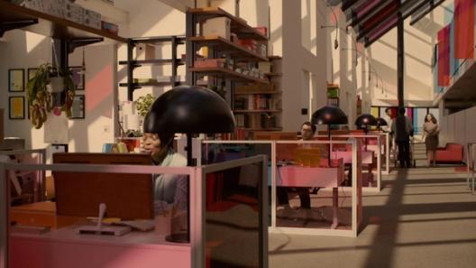 A bright, open-plan office with pink cubicles, bookshelves, and colorful glass panels glows in warm sunlight.