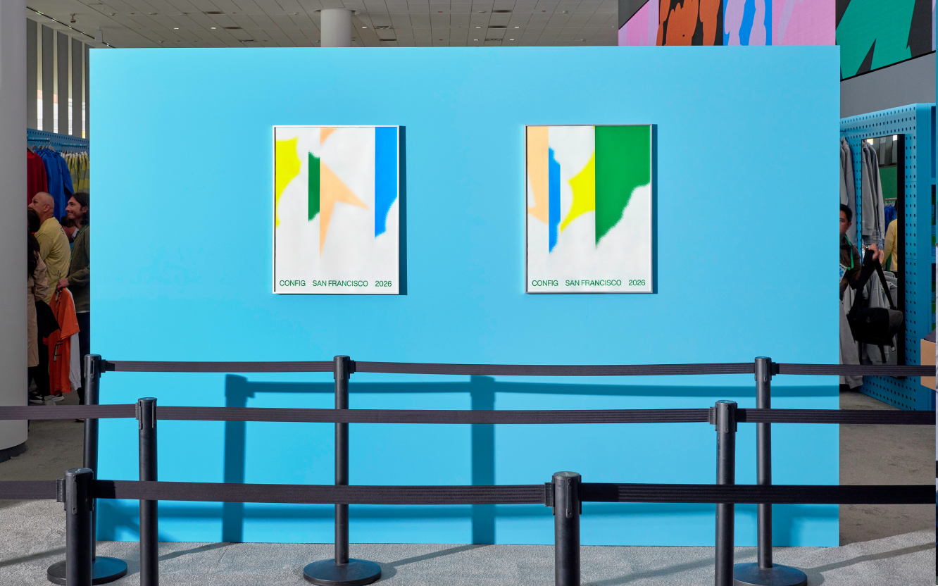 Two abstract "Config San Francisco 2026" posters hang on a bright blue wall behind stanchion barriers