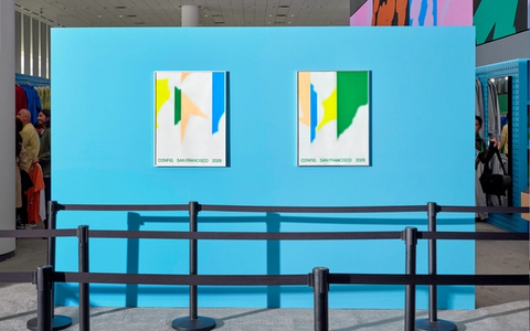 Two abstract "Config San Francisco 2026" posters hang on a bright blue wall behind stanchion barriers