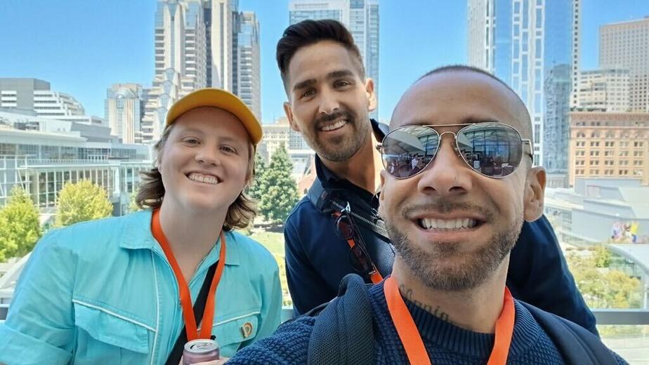 Three people smile for a selfie with downtown San Francisco in the background.