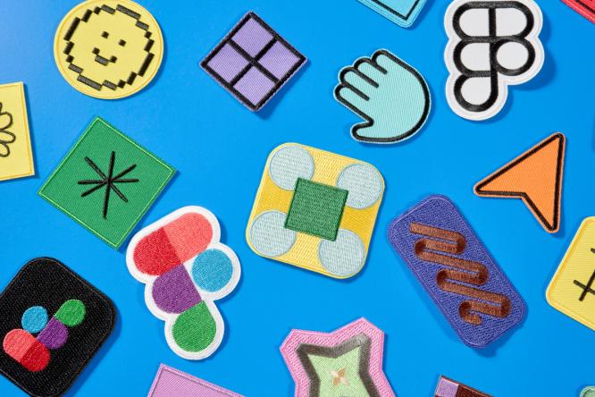 There are 16 patches scattered randomly across a blue surface. Each patch is embroidered with a different design and with multiple colors. Some are abstract shapes, some are UI, and three are the Figma logo.