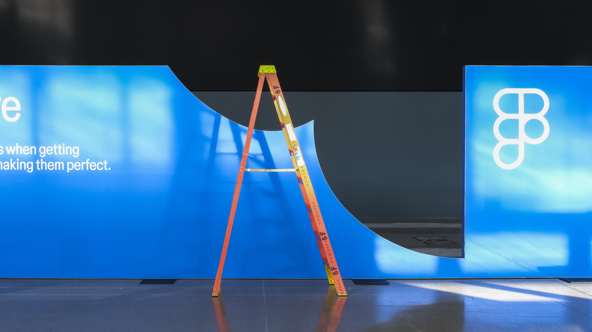 Blue Config display wall with brand logo partially assembled, as orange ladder stands in center.