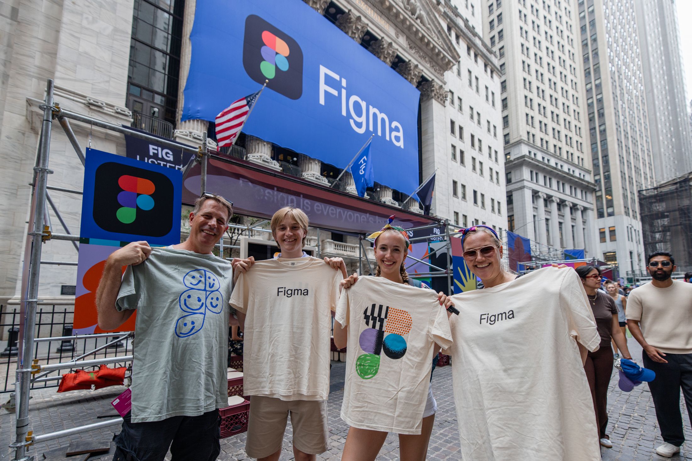 Four people hold up Figma T-shirts in front of the New York Stock Exchange during the event.