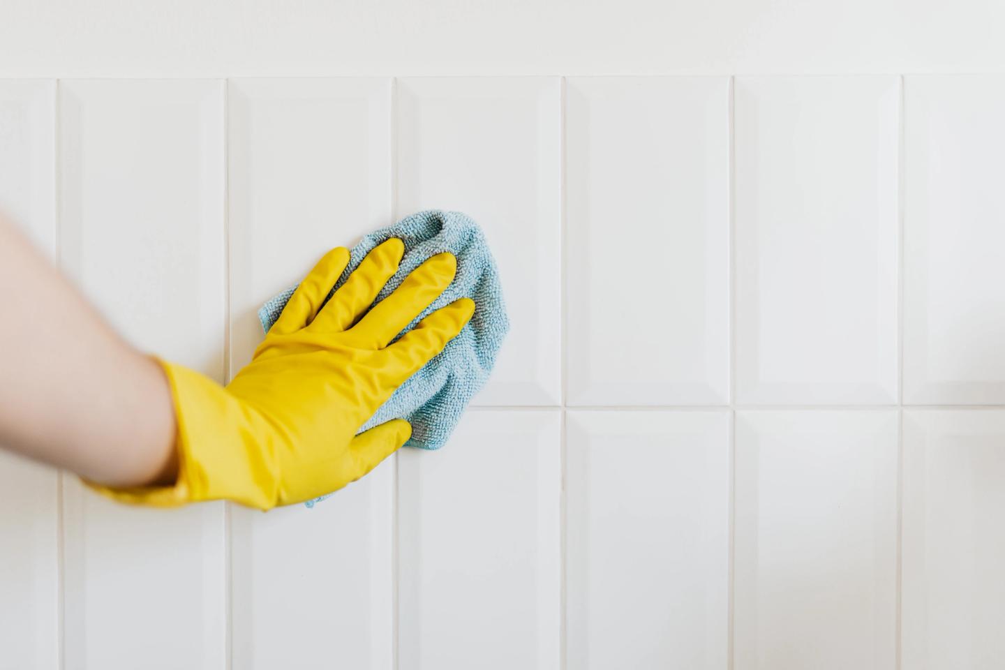 hand in rubber glove cleaning tiles using microfibre cloth