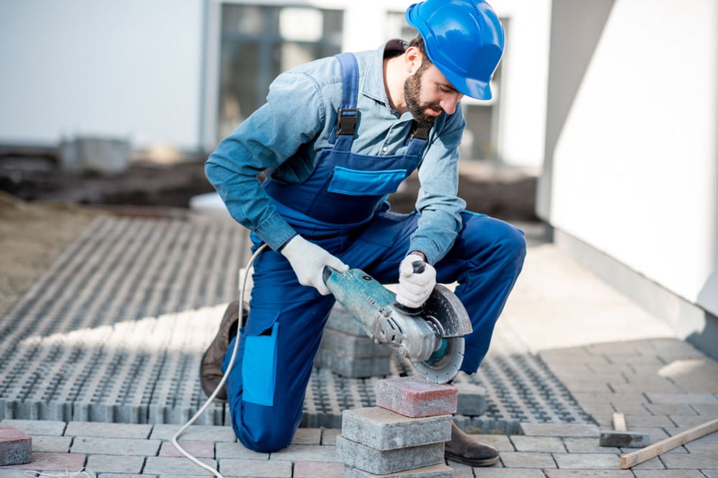 man in overalls and safety helmet cutting paving slabs using masonry saw