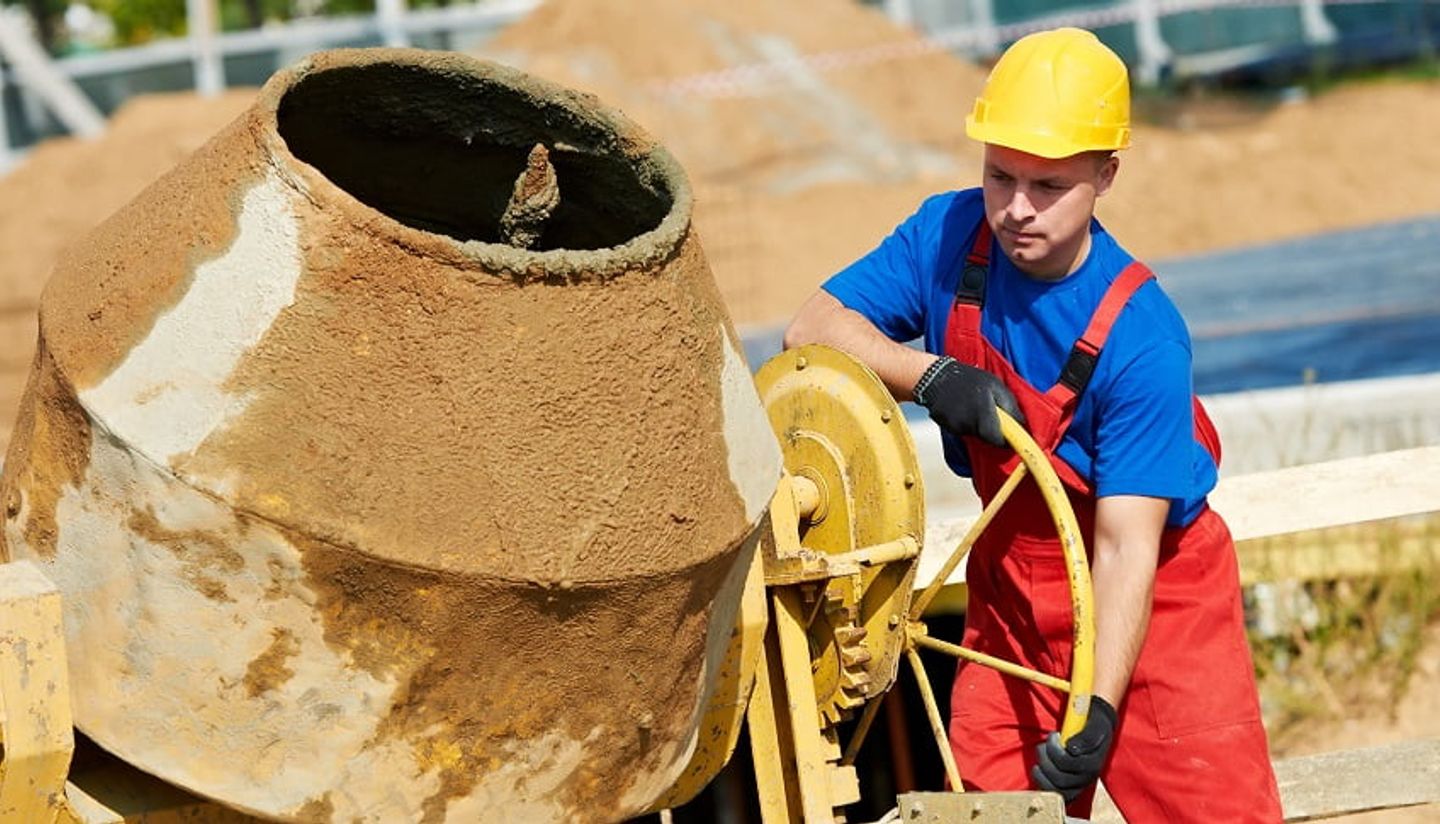men in a safety helmet using a concrete mixer on a building site