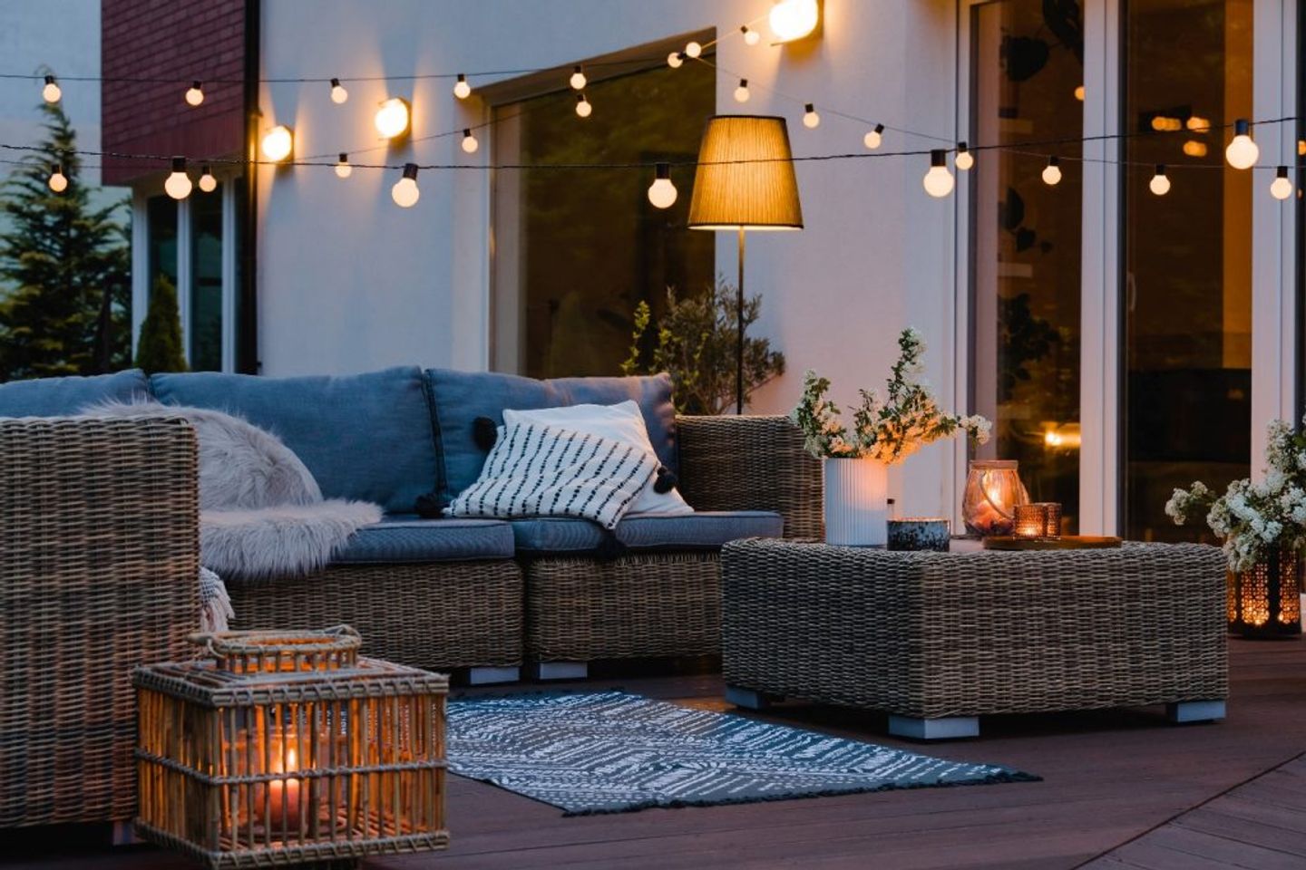 back of the house garden patio with rattan furniture carpet overhead string bulb lights and a floor lamp