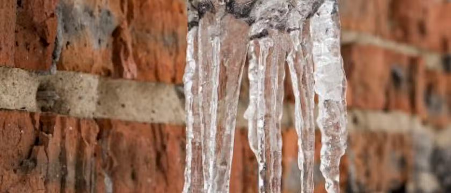 Icicles coming out of a frozen pipe at the side of a house.