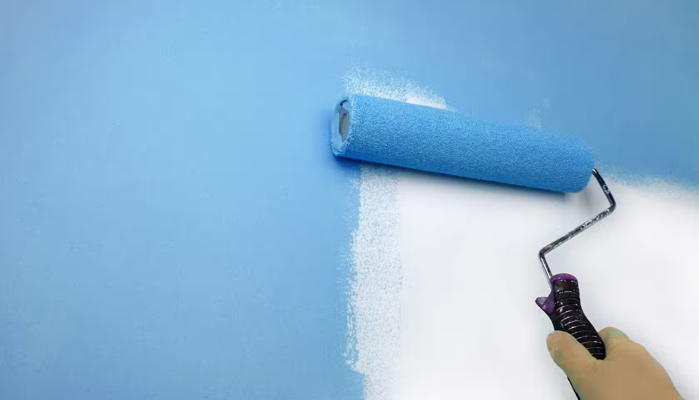 Someone using a roller to paint a wall blue