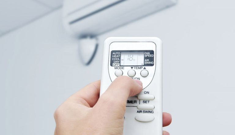 Hand on the air conditioner unit remote control turning it on during hot summer weather