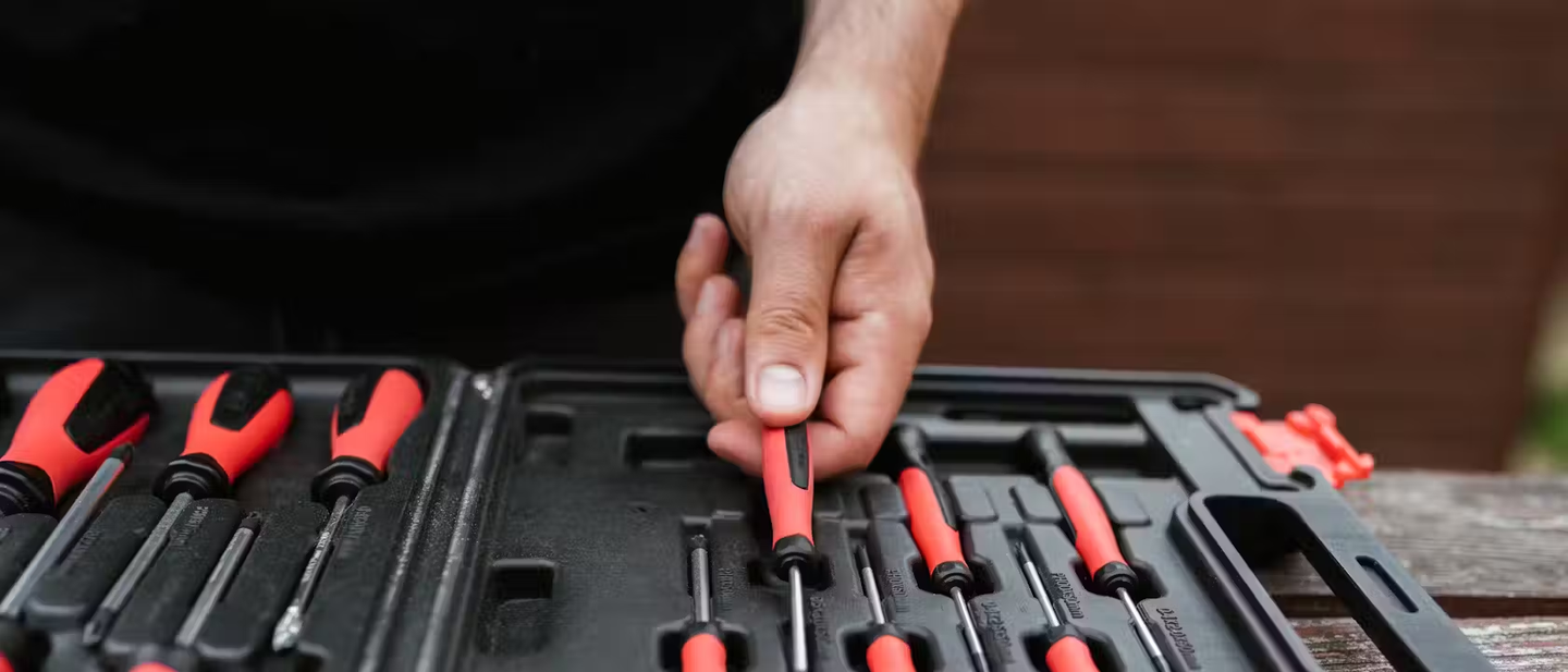 Someone choosing an insulated screwdriver from a tool kit.