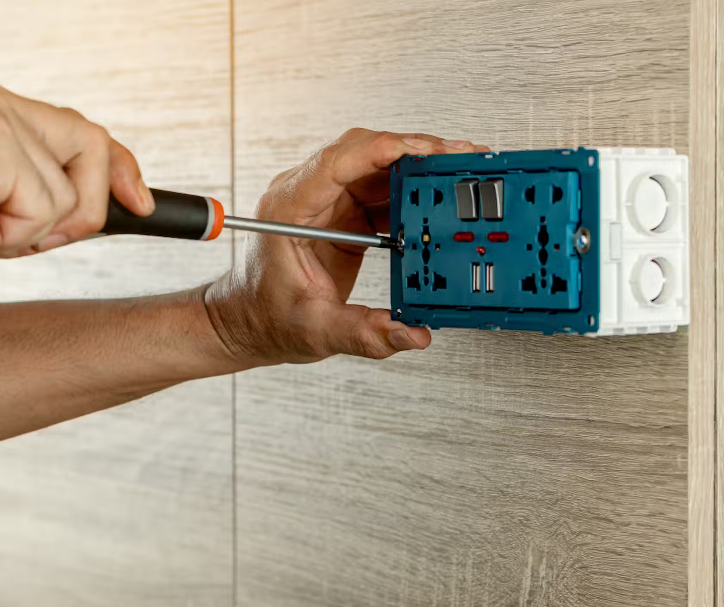 A socket being screwed back into the wall with an insulated screwdriver.