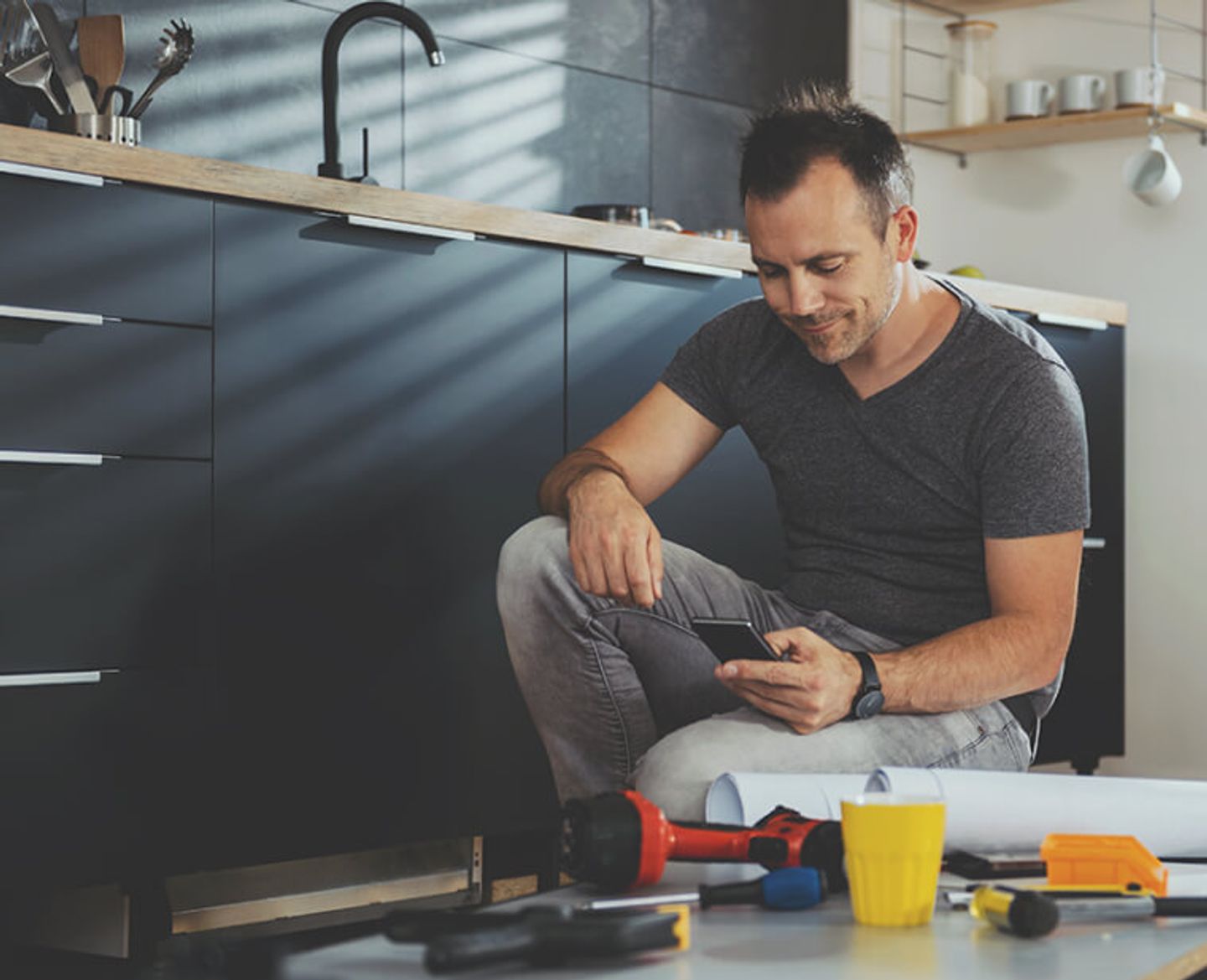 man checking his phone while working on a diy project in the kitchen