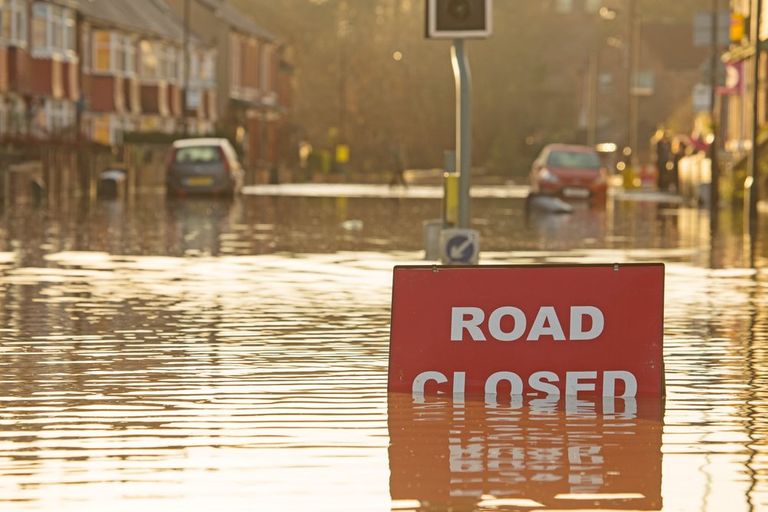 A flooded British street with a Road Closed sign in the foreground and houses and cars in the background