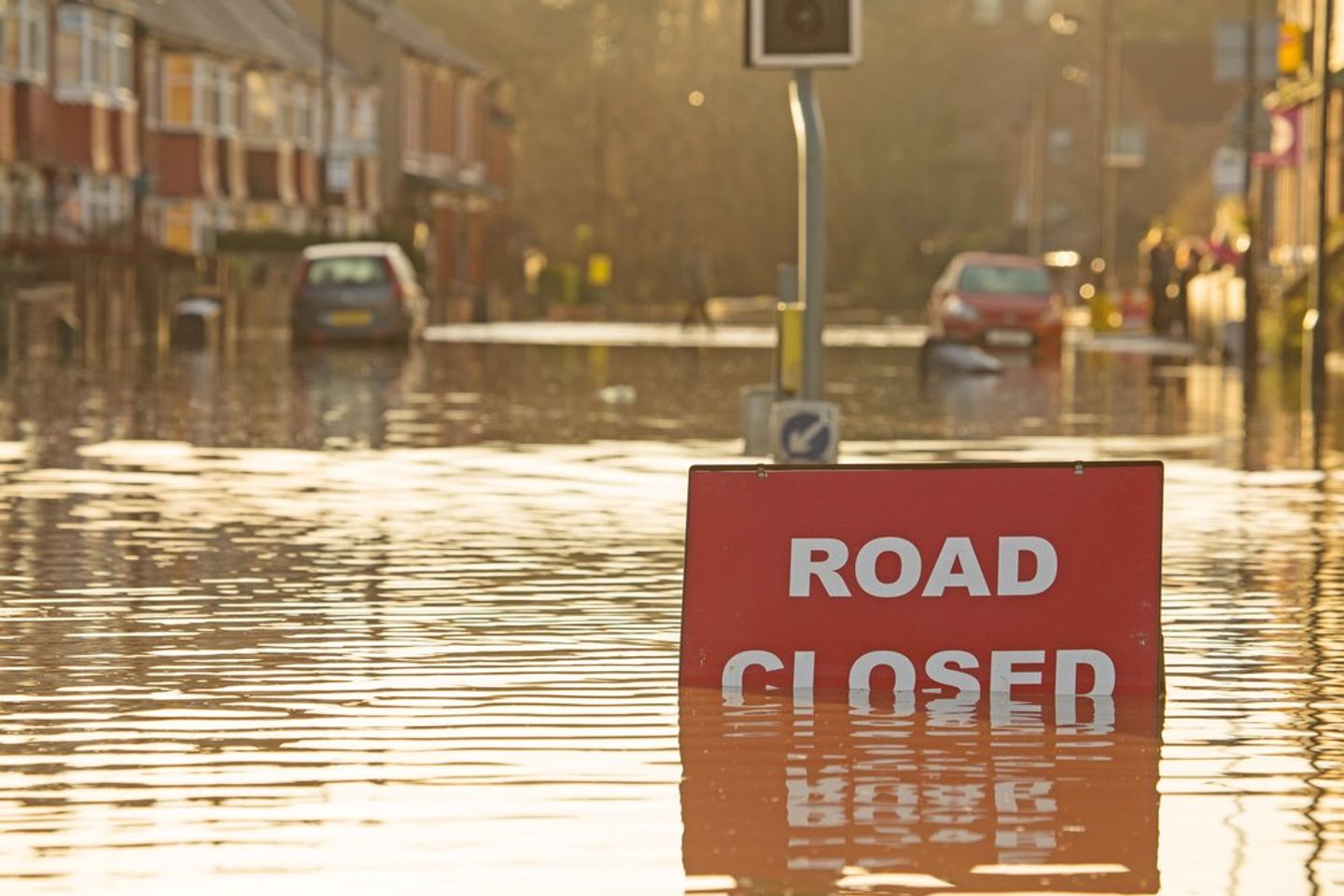 A flooded British street with a Road Closed sign in the foreground and houses and cars in the background