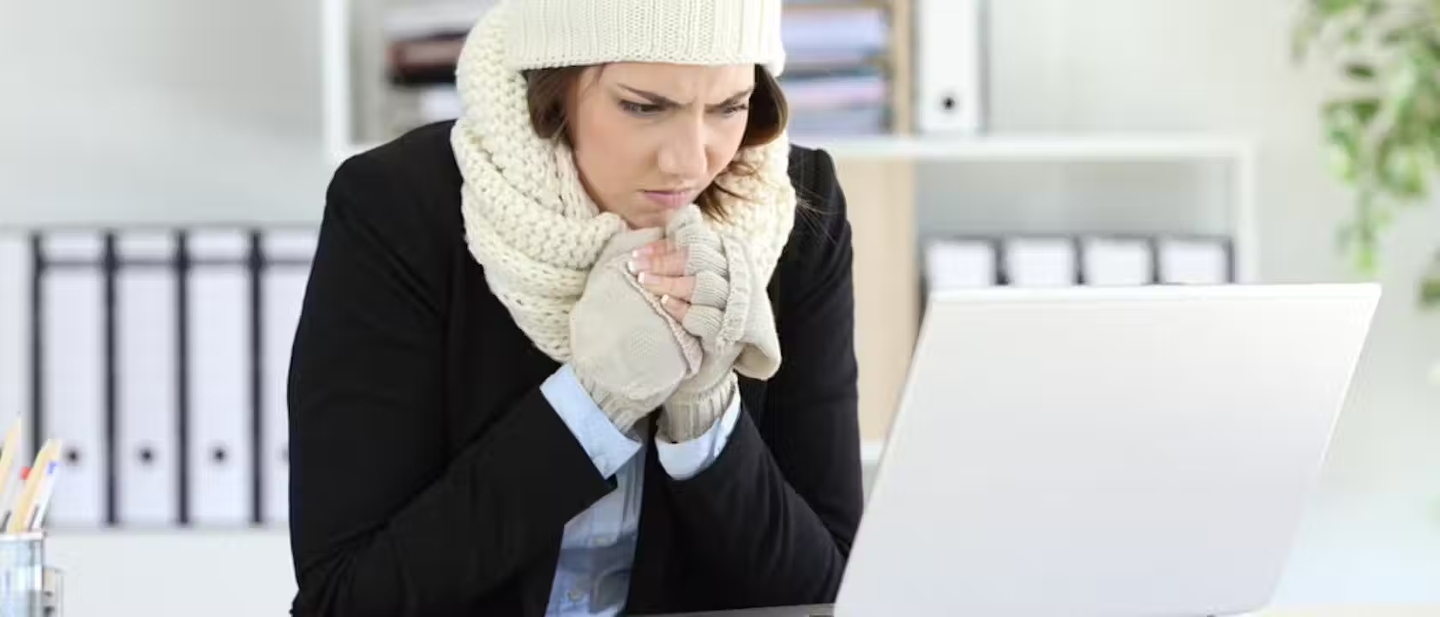 Woman wearing a woolly hat, scarf & gloves whilst working in the office