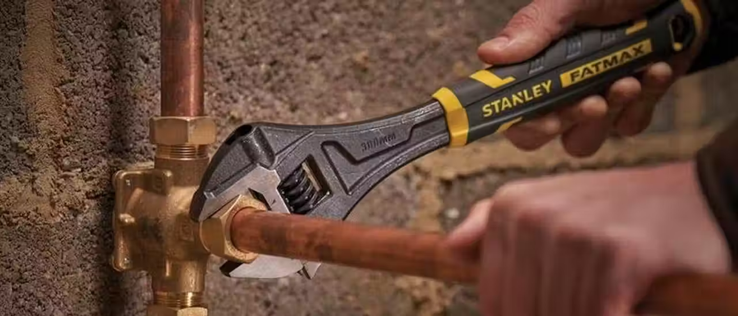Someone using a Stanley FatMax wrench on a copper pipe.