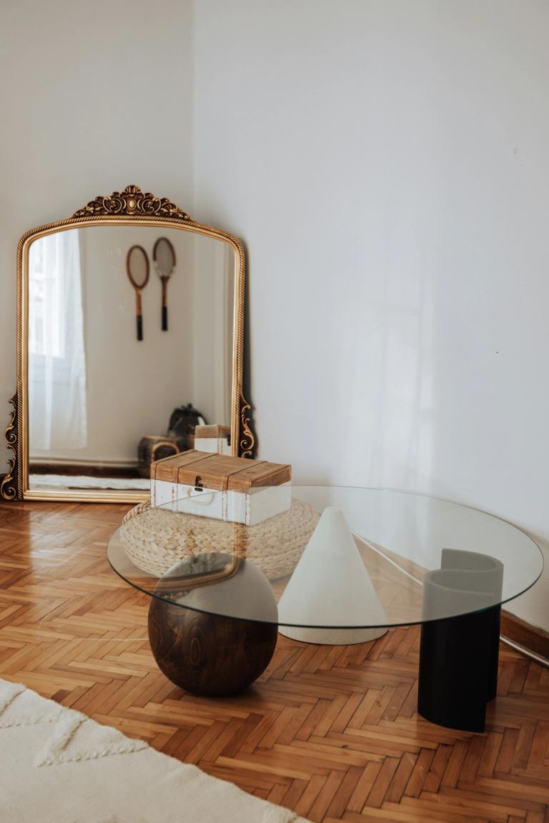 Finished herringbone flooring with an ornate mirror and glass table