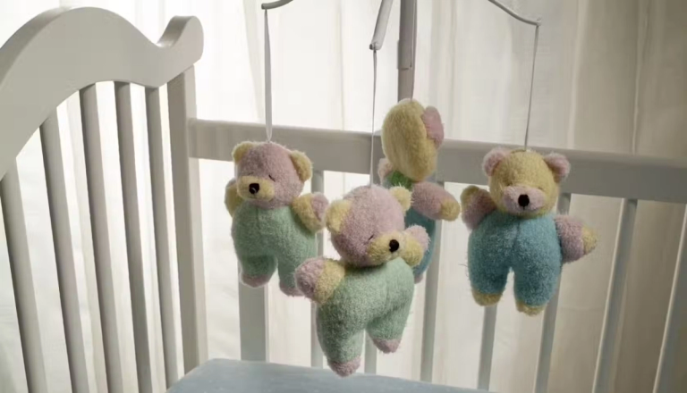 A baby's crib with a teddy bear cot mobile.