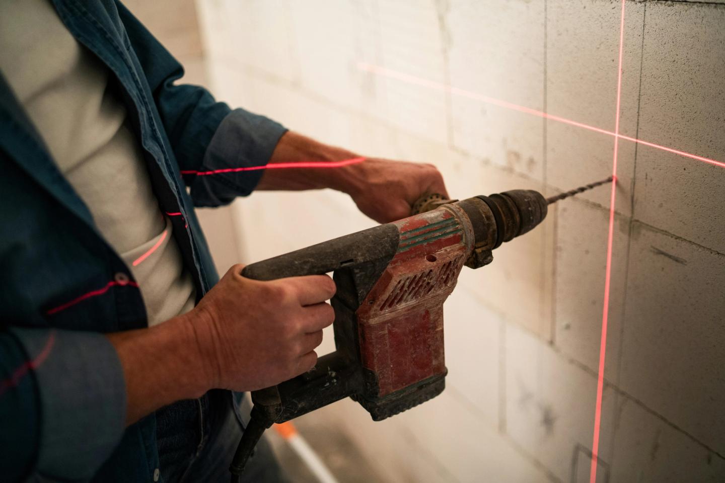 Someone drilling into the wall whilst using a cross line laser level.